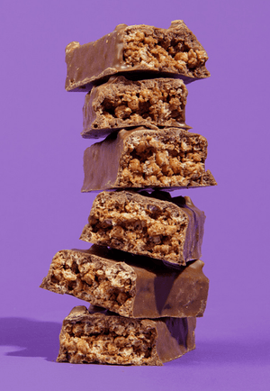 Stacked chocolate-covered snack bars with crispy layers on a purple background.